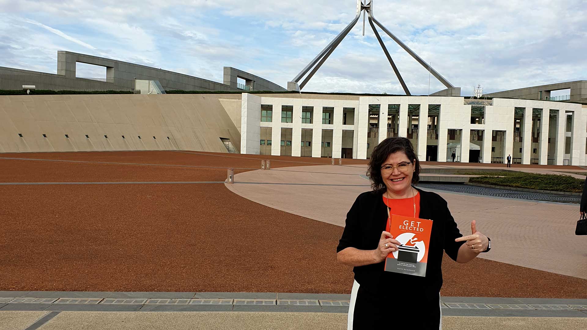 Ruth McGowan holding her book Get Elected outside Parliament House in Canberra