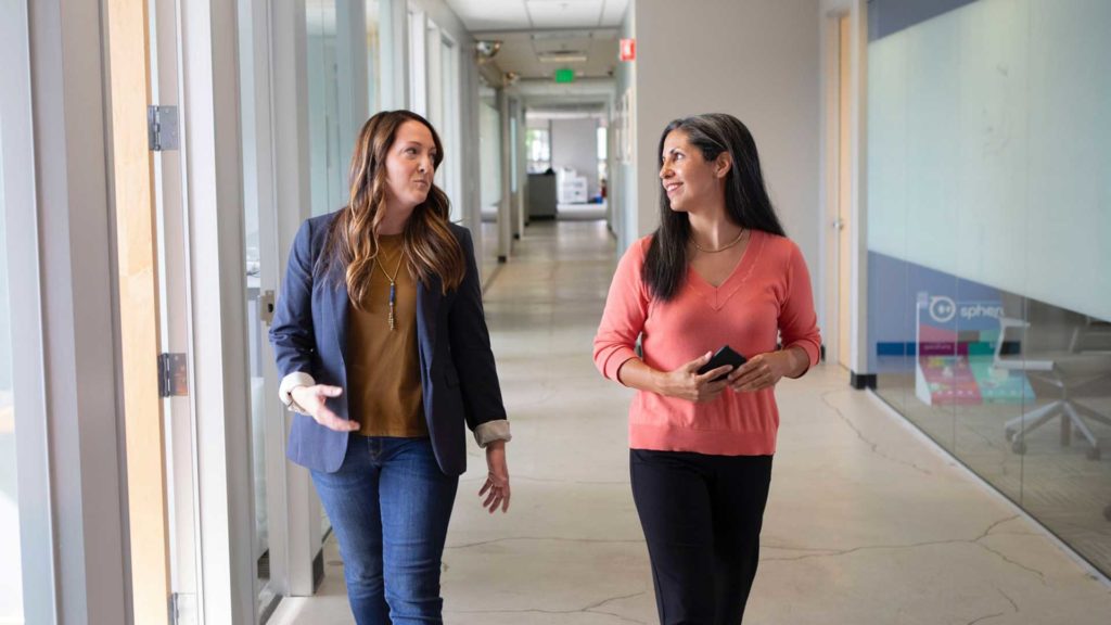 Two women talking while walking down a large hallway
