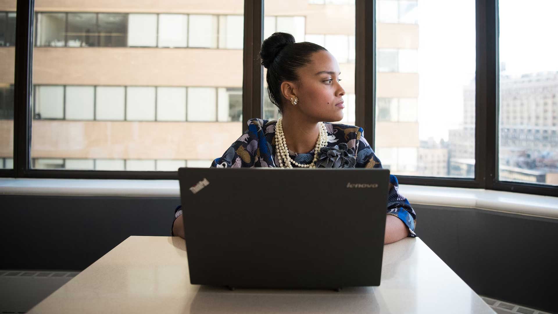 Woman with a laptop in an office environment. She is gazing into the distance.