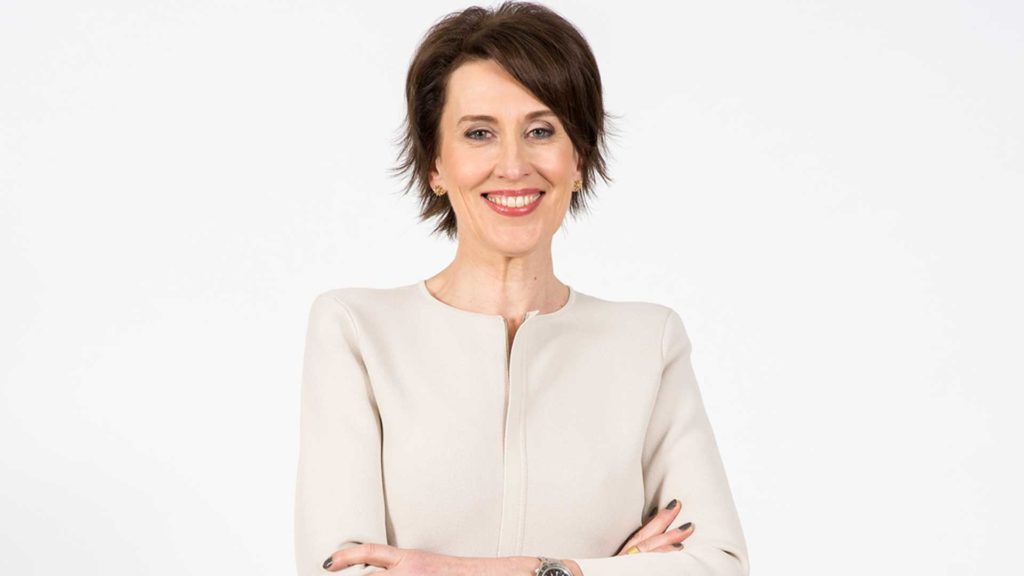 Photo of Virginia Trioli, smiling, wearing a white blouse against white background