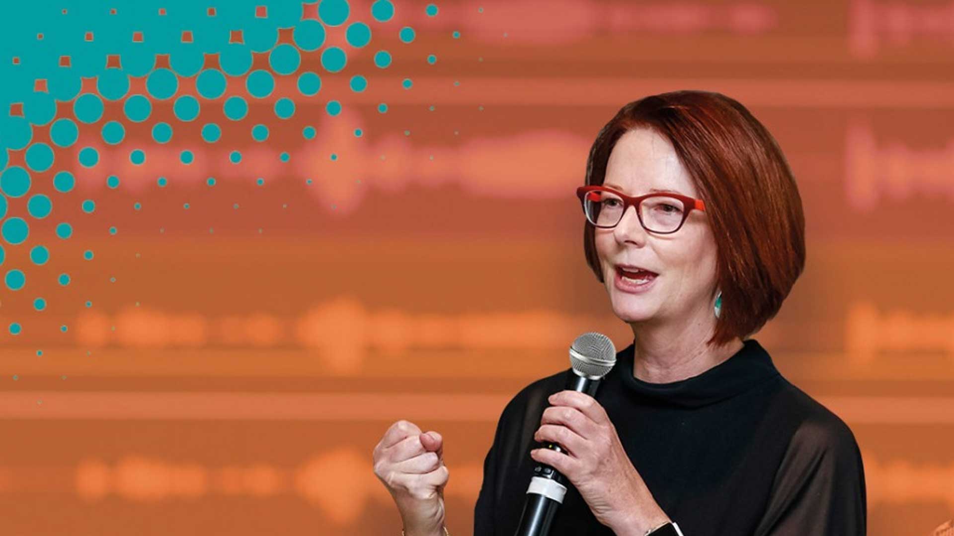 Julia Gillard speaking into a microphone against an orange backdrop