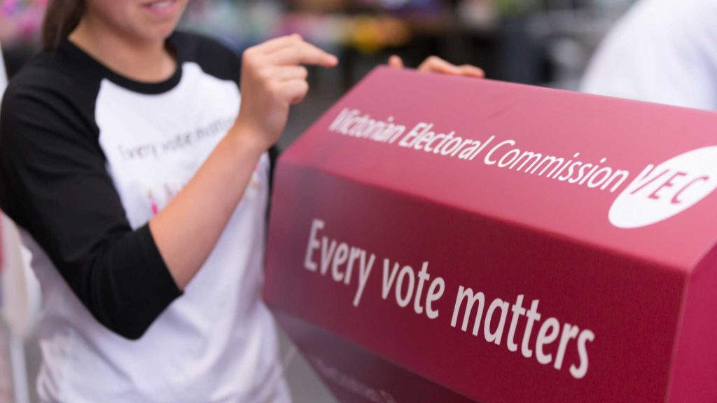 Woman posting card into a red Victorian Electoral Commission box with "Every vote matters" written on the side