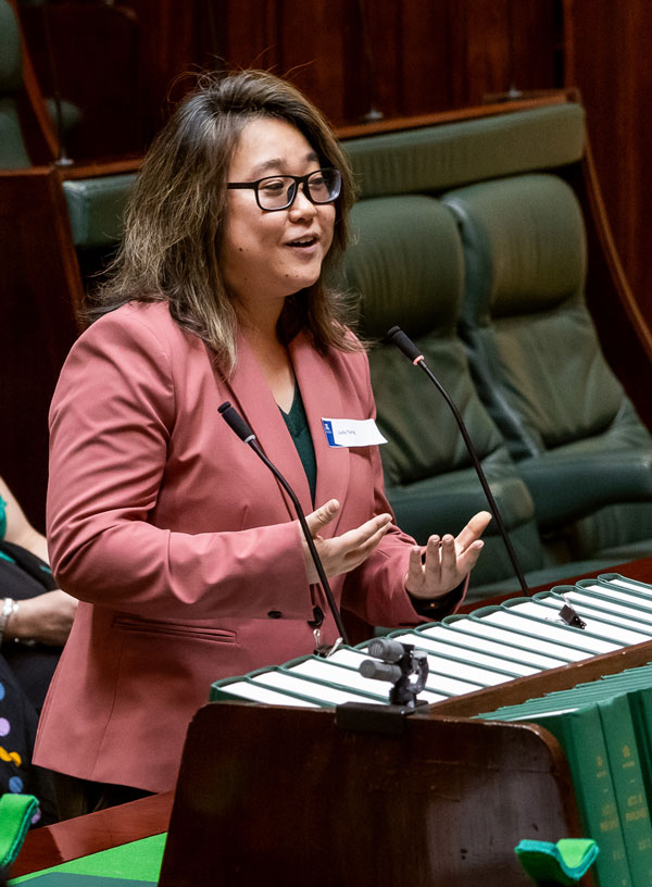 Dr Judy Tang wearing a pink blazer, delivering a speech in parliamentary chambers