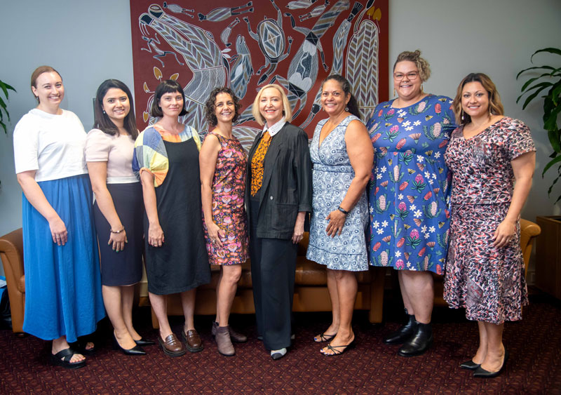 Diverse group of smiling women posing in front of a large Aboriginal artwork