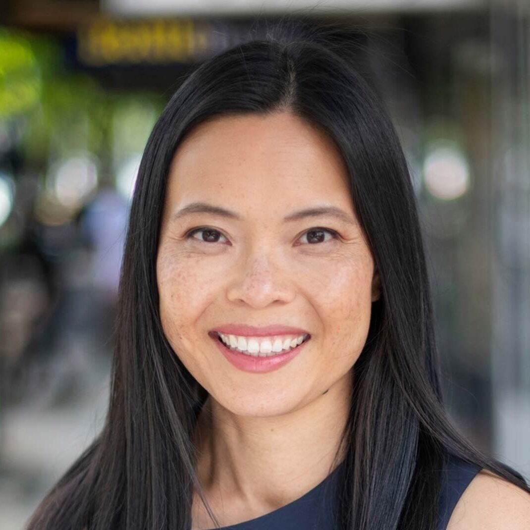 Photo of Sally Sitou MP smiling, suburban shopping strip in the background