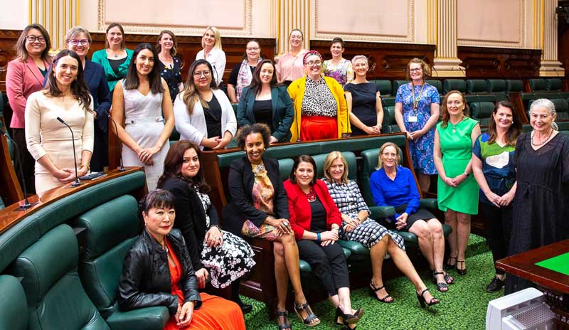 Large group of diverse women smiling, posed standing in Victorian parliamentary chamber