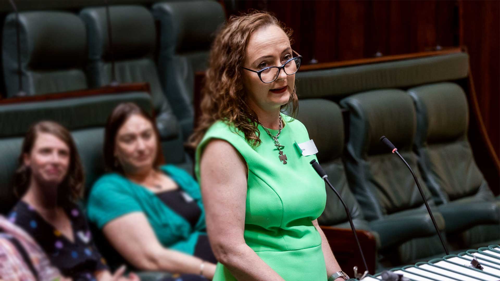 Mary Doyle wearing a green dress giving a speech in Victorian Parliament