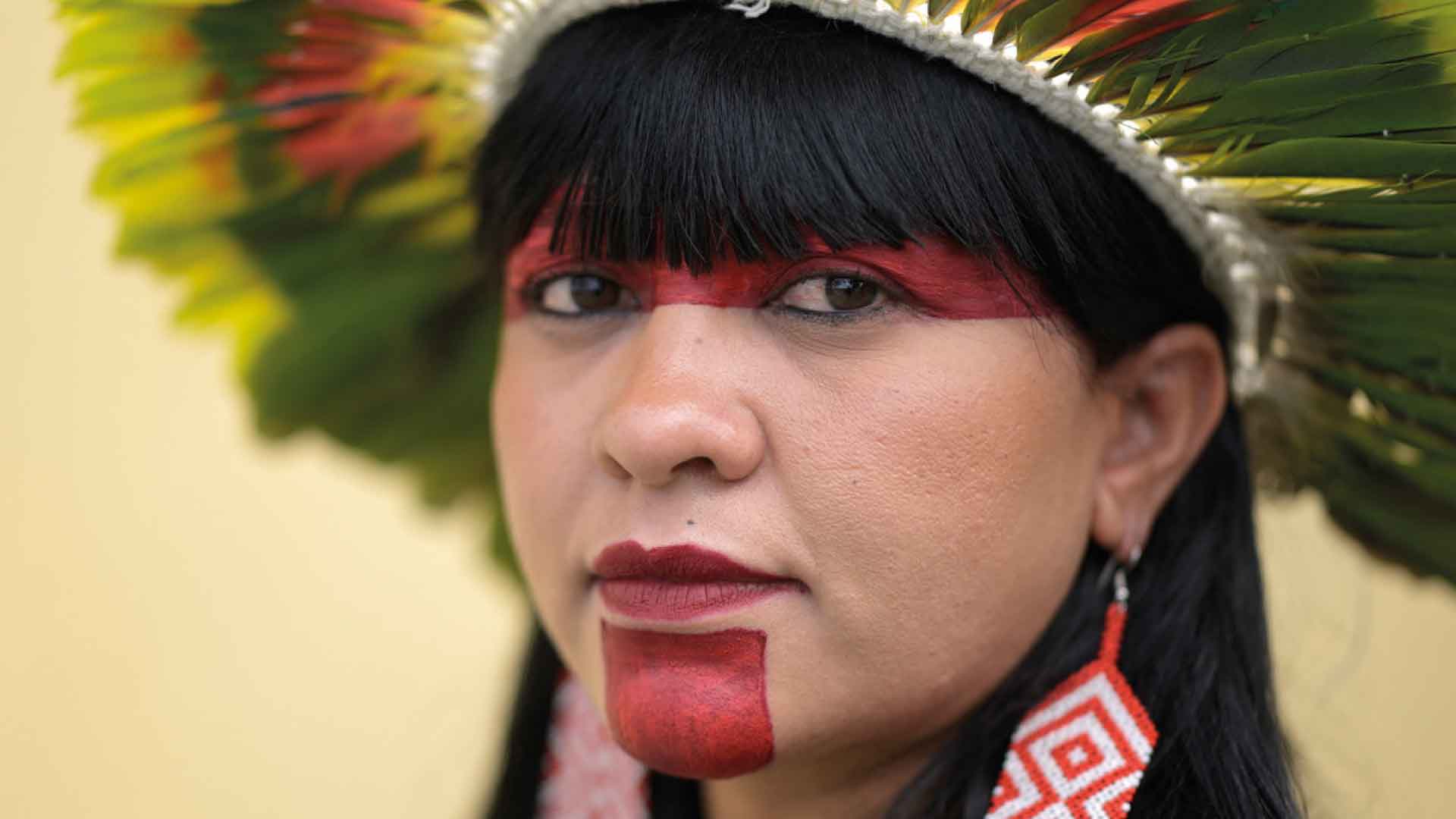Photo of a woman wearing tribal headdress, large earrings and red paint across her eyes and chin