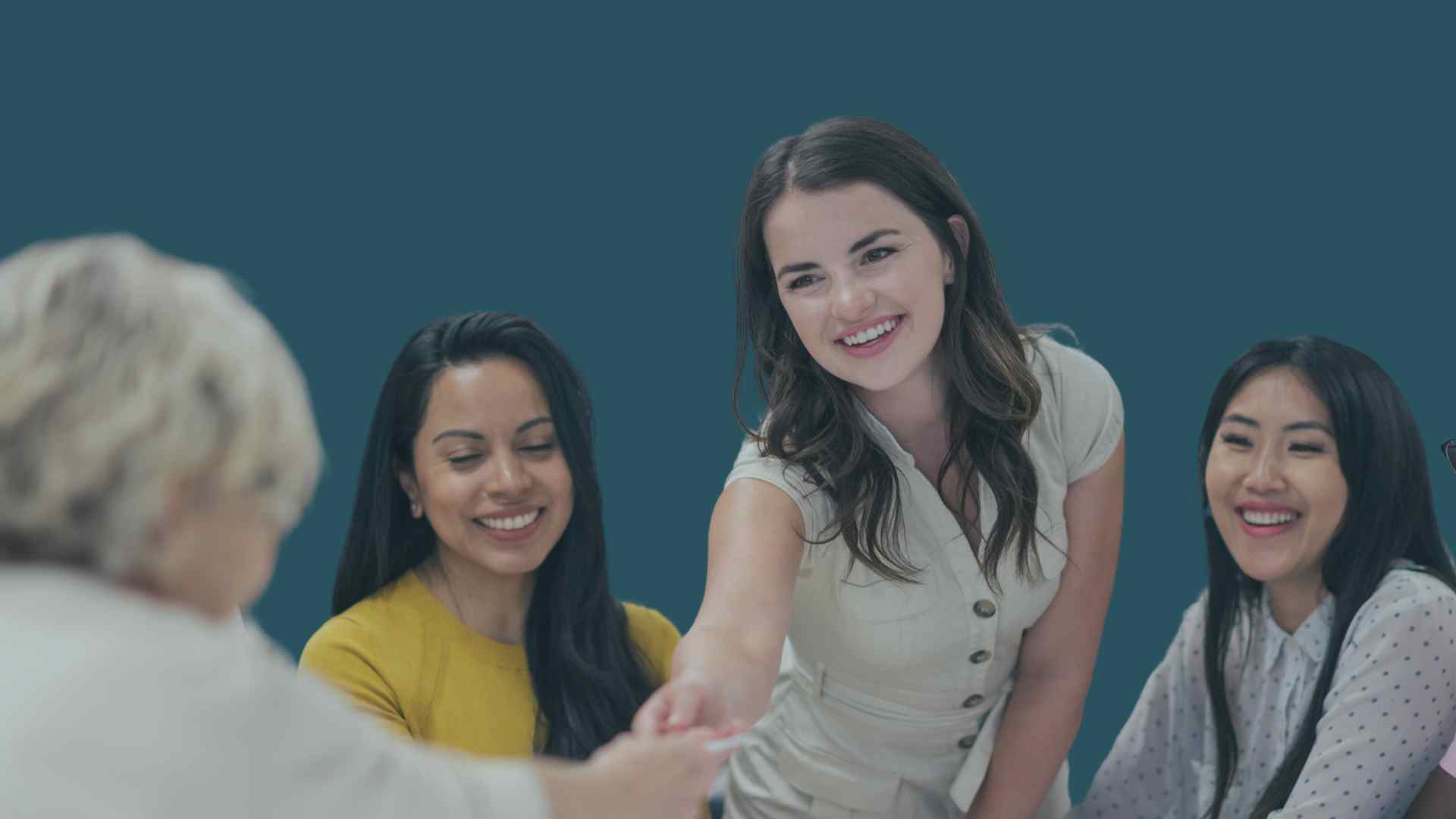 Four diverse women smiling, two of them shaking hands