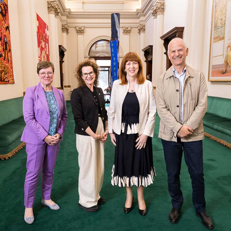 Photo of University of Melbourne Provost Nicola Phillips, Carol Schwartz AO, Her Excellency Margaret Gardner, and Alan Schwartz. They are standing in a grand hallway with green carpet.