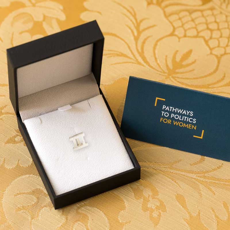 Close up of a silver pin in a black jewellery box, with a blue Pathways to Politics card propped next to it