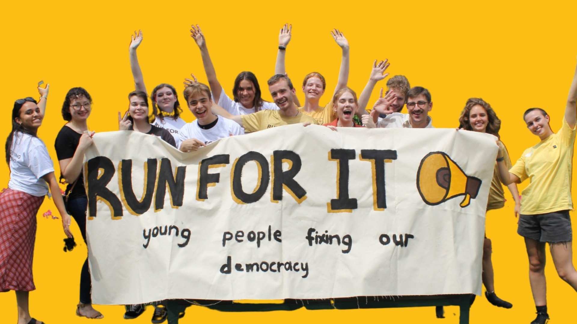 Group of young people holding up a large fabric sign reading "Run for it: young people fixing our democracy" against a bright yellow background