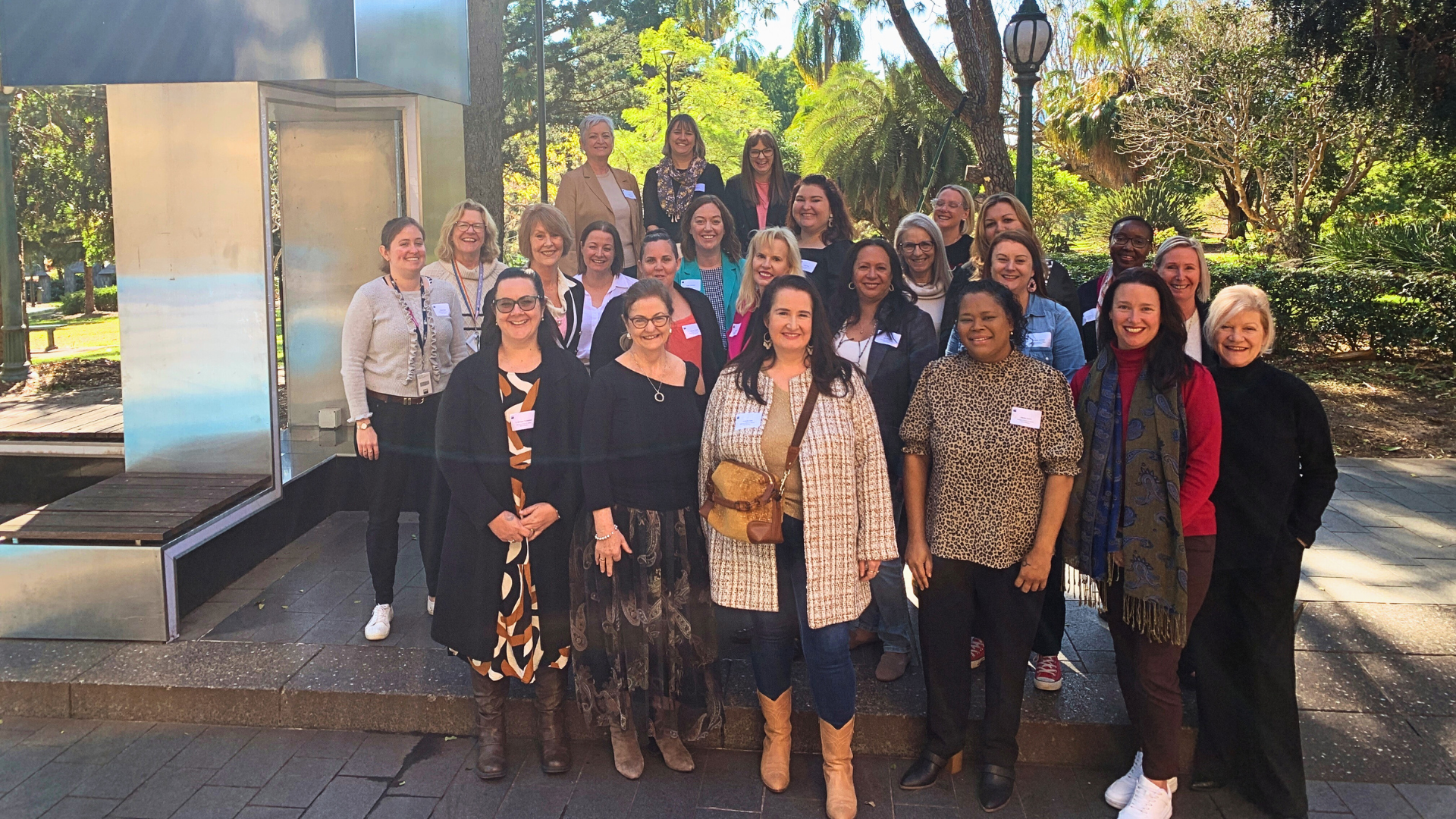 A group of 20 or more diverse women stand posing smiling outside in the winter sun