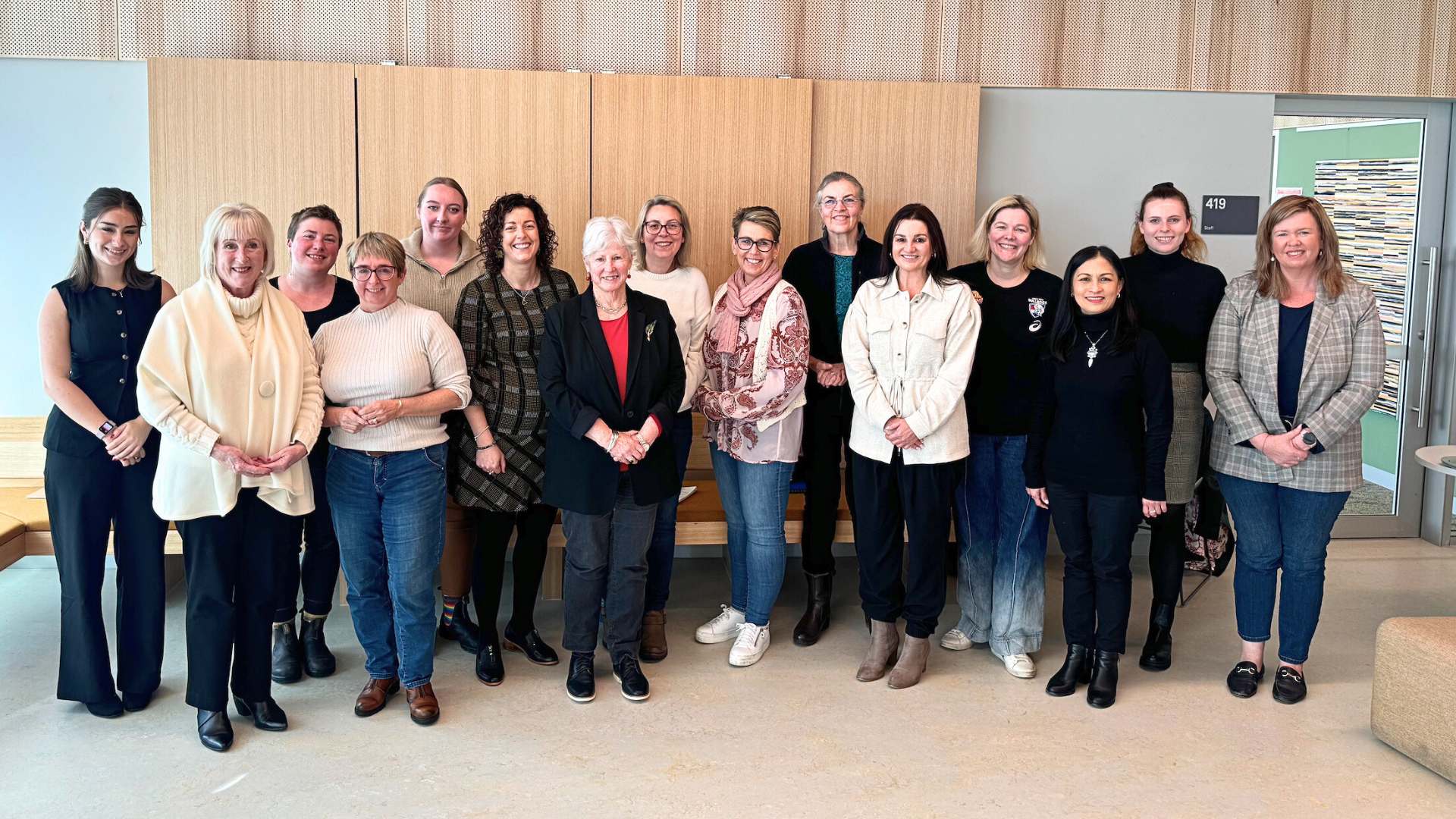 Group of 15 diverse women posing for a photo in a modern conference-style room