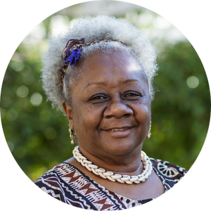 Photo of a smiling black woman with grey hair, wearing a patterned top and necklace