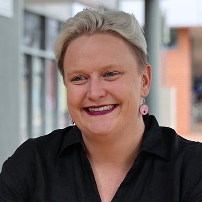 Photo of Heidi Prowse, a white woman with short bleached blond hair. She is smiling and wearing a black shirt.