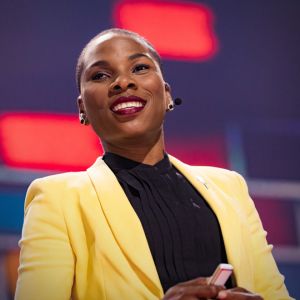 Photo of Luvvie Jones, a young black woman wearing a yellow blazer, smiling