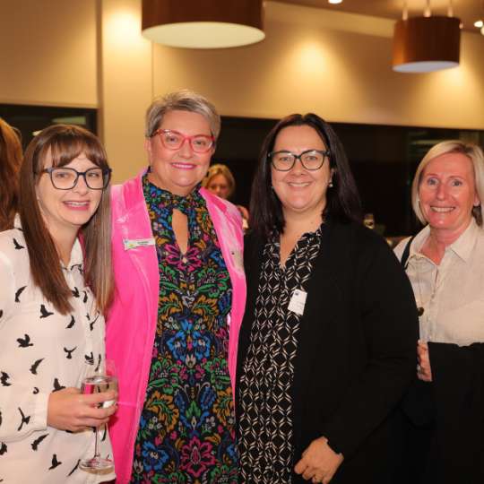 Four smiling women wearing business wear, with nametags.