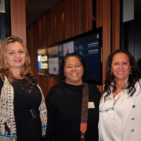 Three smiling women wearing black and white professional outfits. They are wearing name tags.