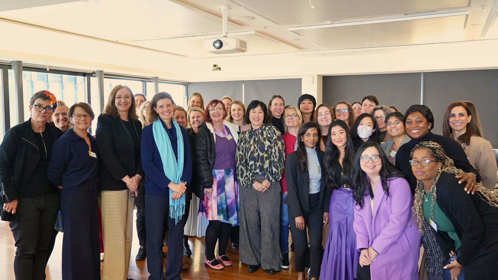 Large group of diverse women pose for a photo together in a conference-style room