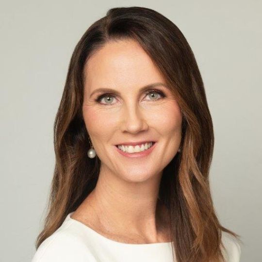 Photo of a smiling white woman with long, light brown hair, against a plain grey background