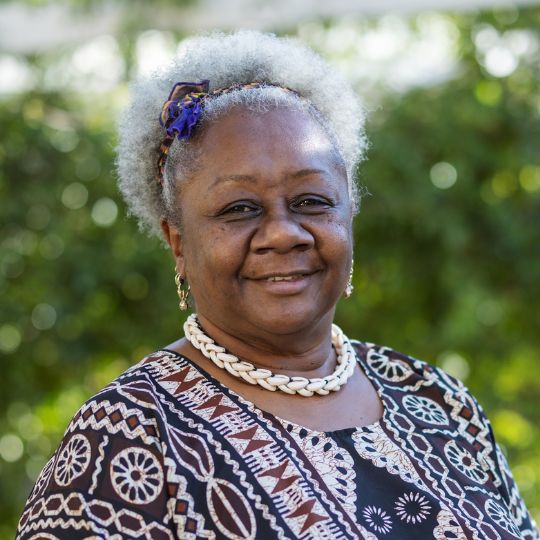 Photo of a smiling black woman with grey hair, wearing a patterned top and necklace