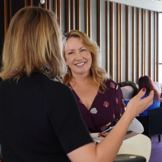 Photo of two blonde women standing having an animated conversation