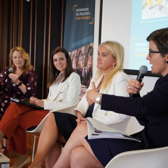 Four women sitting panel-style. One is speaking into a microphone/