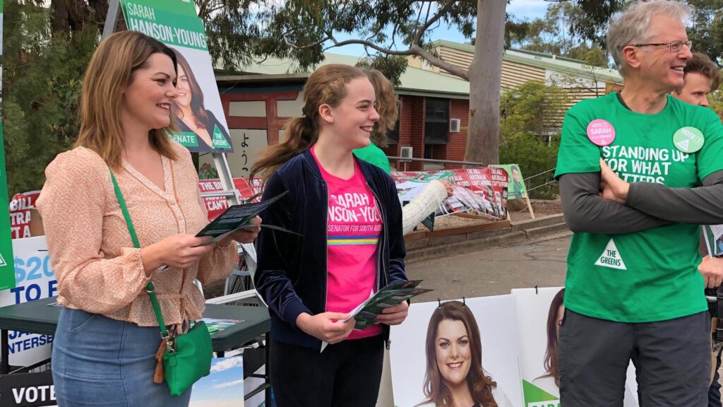 A woman, teenage girl and older man outdoors, holding pamphlets for The Greens