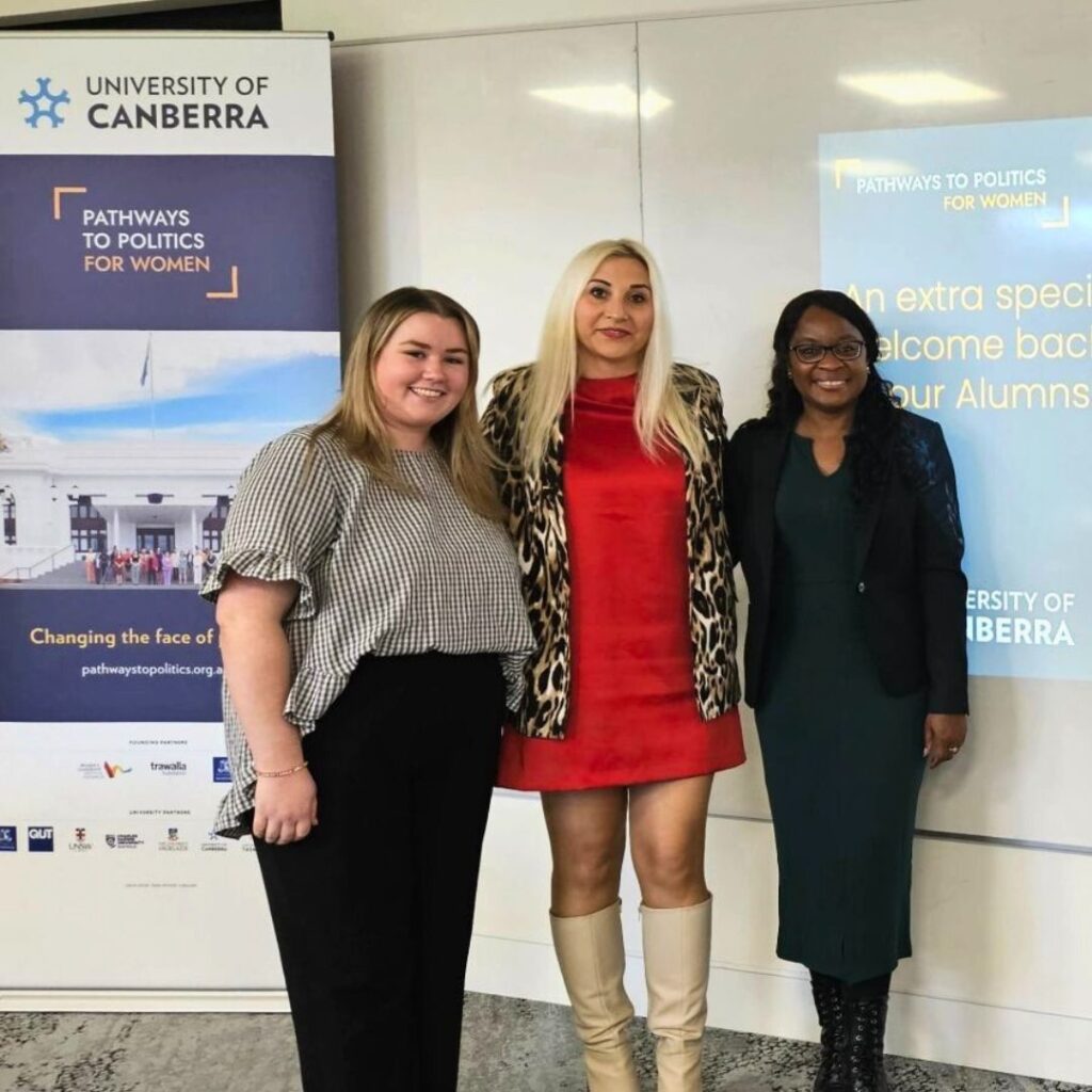 Three women standing in front of a University of Canberra Pathways to Politics banner