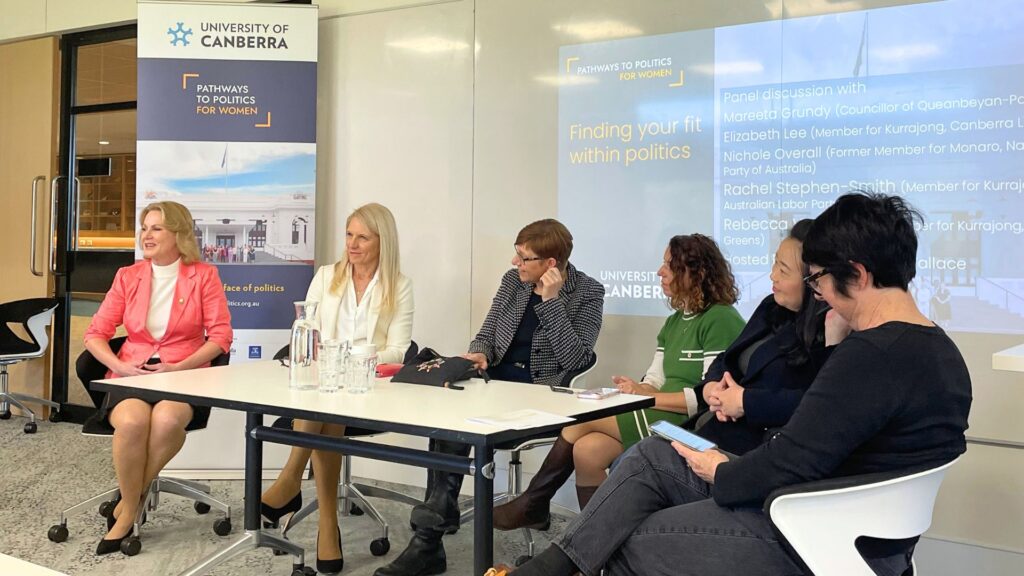 Six diverse women seated behind a white table, in conversation