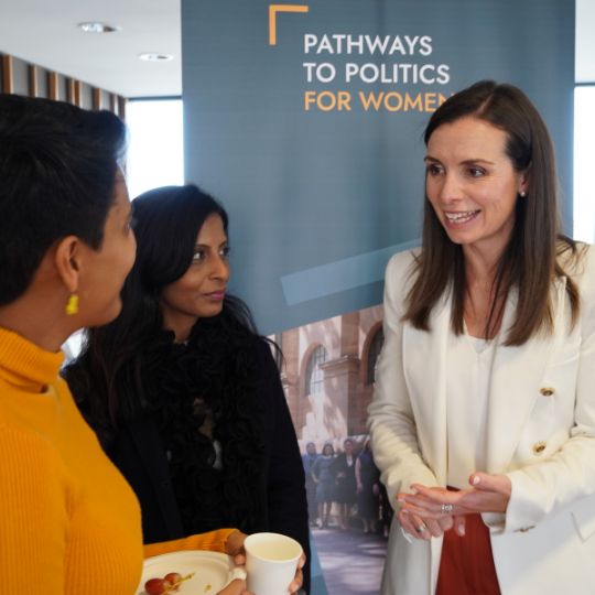 3 diverse women chatting in front of a dark blue banner with the Pathways to Politics logo on it