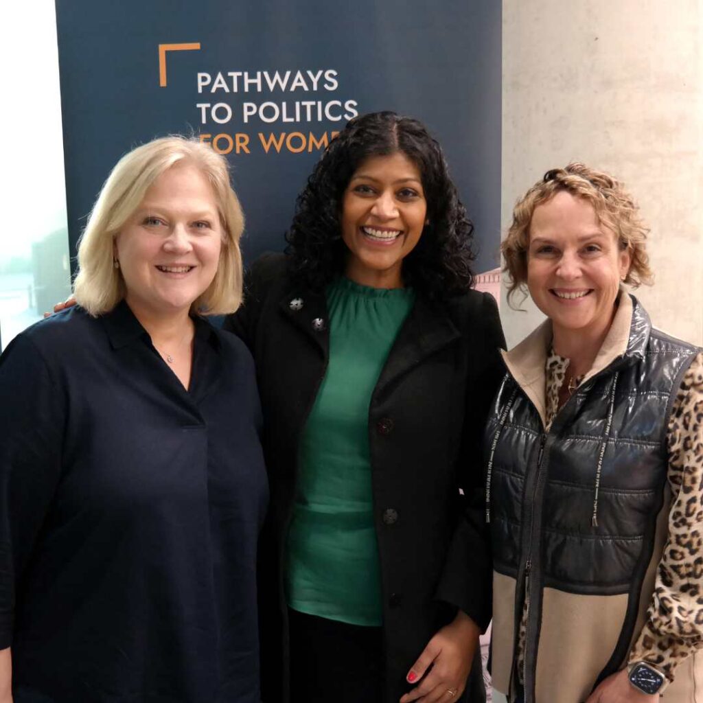 Photo of three women smiling for a photo in front of a dark blue Pathways to Politics banner