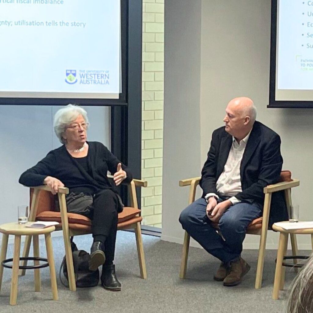 Photo of an older woman and man seated in discussion in front on a projector screen