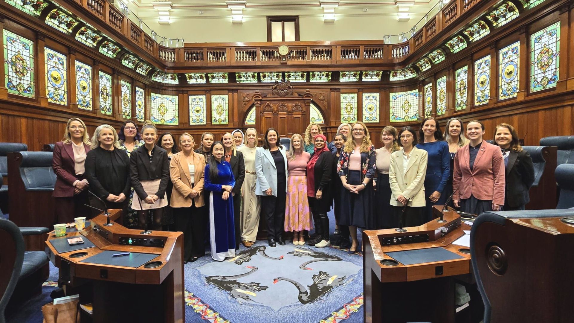 WA cohort, a group of more than 20 diverse women, photographed in a group in parliament chamber, a wood paneled ornate space