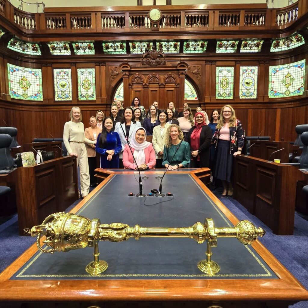 WA cohort, a group of more than 20 diverse women, photographed in a group in parliament chamber, a wood paneled ornate space