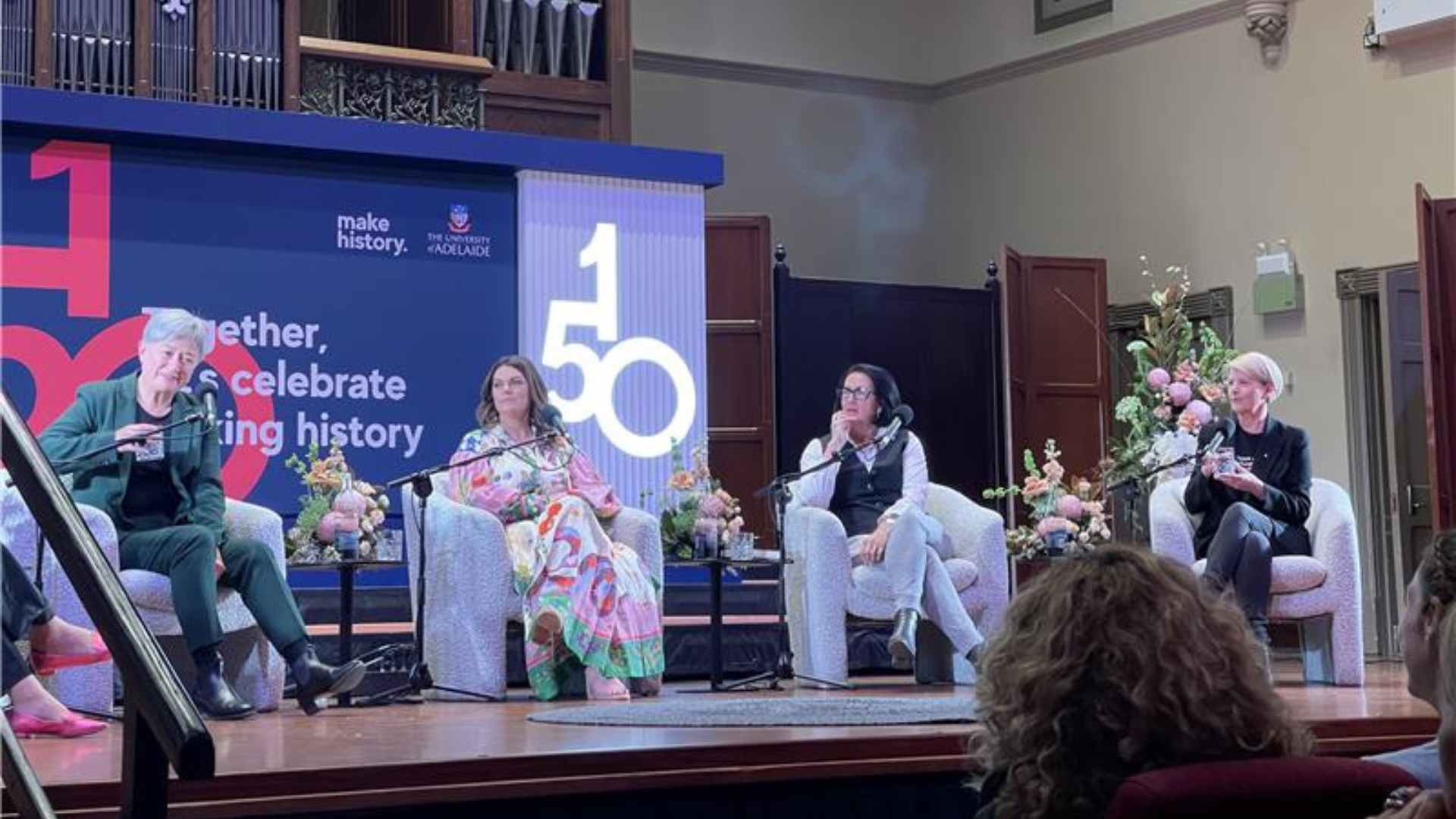 Four women seated on stage, banner with "150" and the University of Adelaide logo behind them