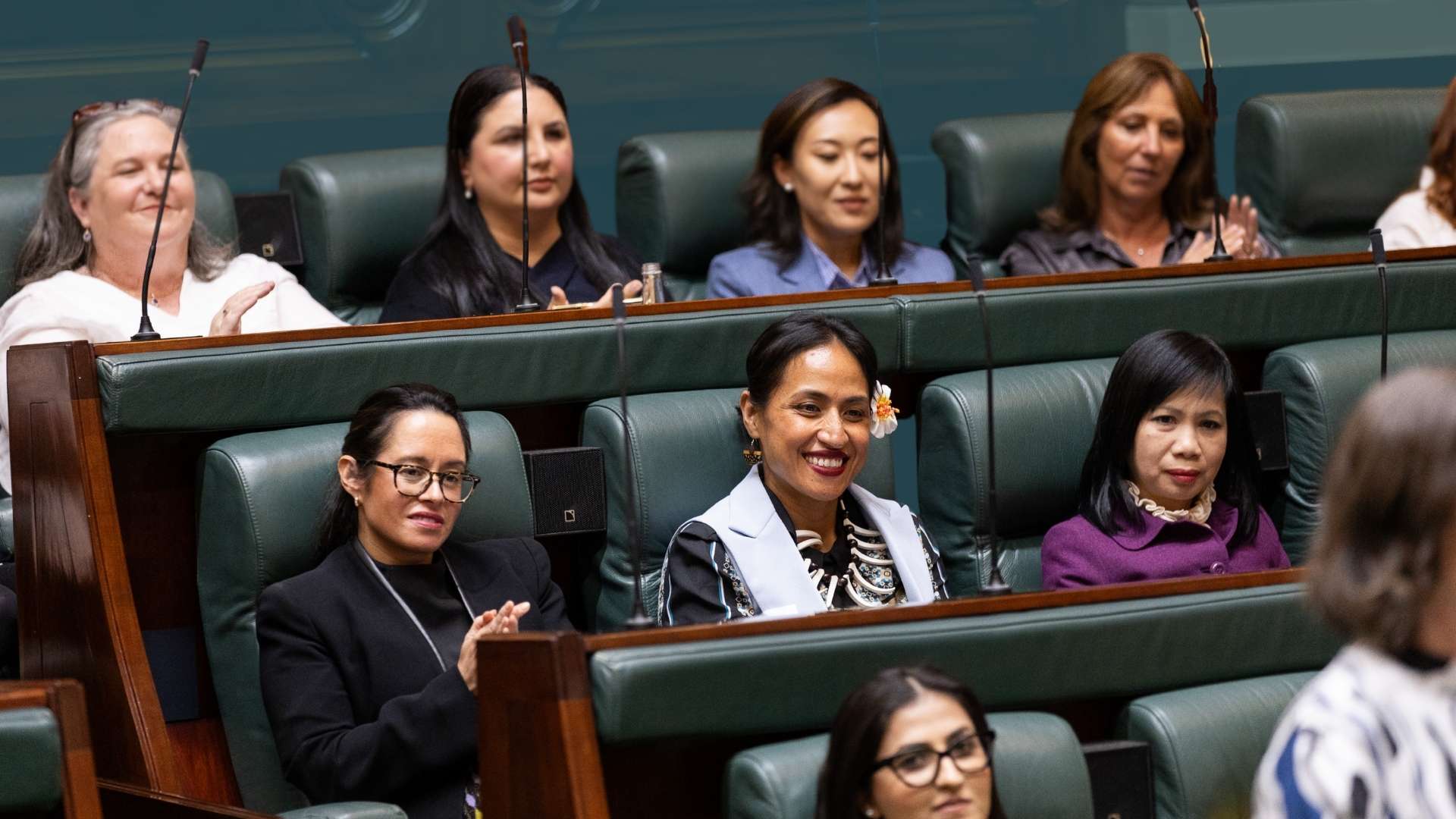 Group of diverse women sitting in green leather bench seats in a parliament chamber.