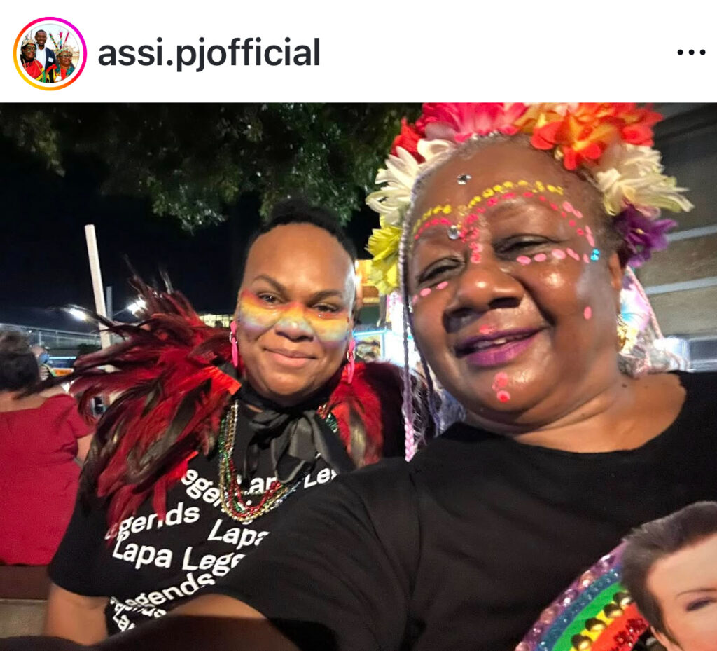 Photo of Emelda Davis wearing face paint and colourful wig. She is with a bald man who has colourful feathers around his neck