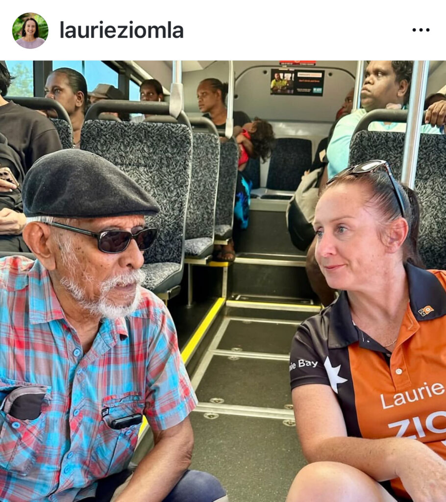Photo of Laurie Zio wearing self branded t-shirt speaking to an older man on a bus