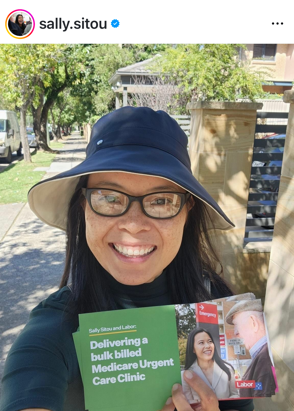 Smiling photo of Sally Sitou wearing sun hat and glasses, holding up political flyer for the camera
