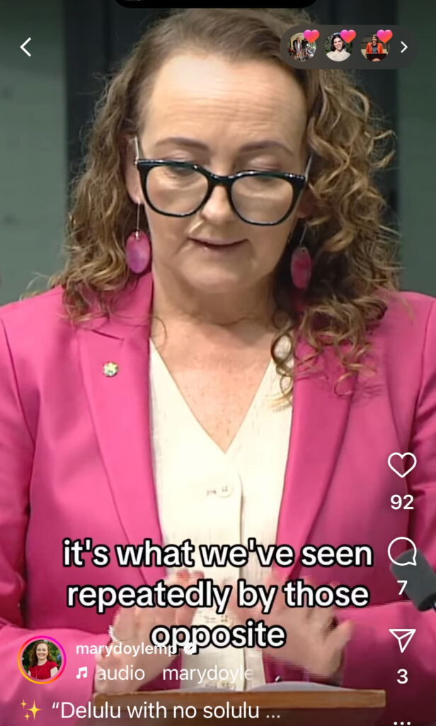 Video still of Mary Doyle reading in parliament wearing a bright pink blazer