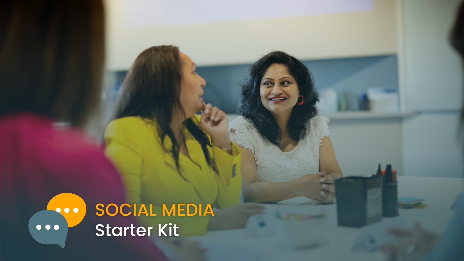 Photo of 3 diverse women sitting in a classroom setting talking and smiling