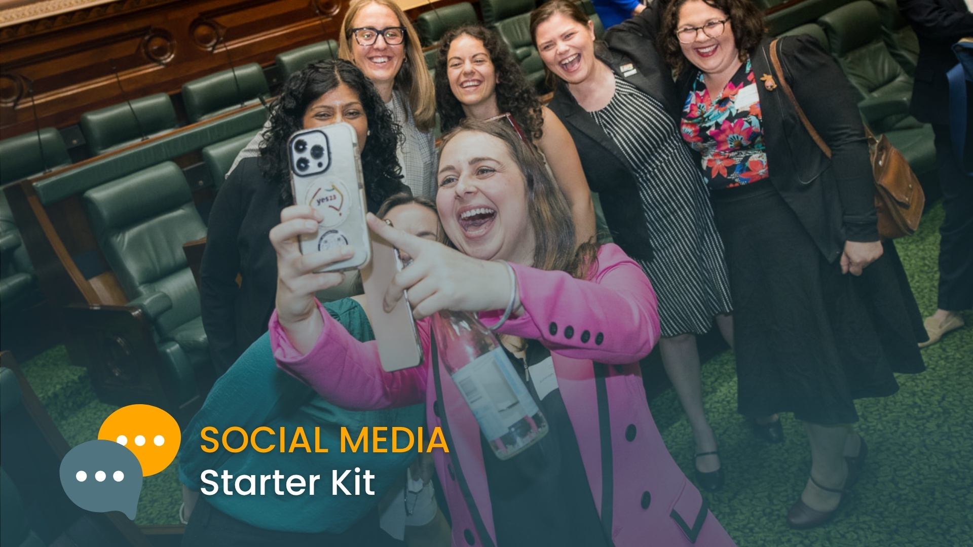 Photo of a group of grinning, diverse women taking a selfie in parliament chamber