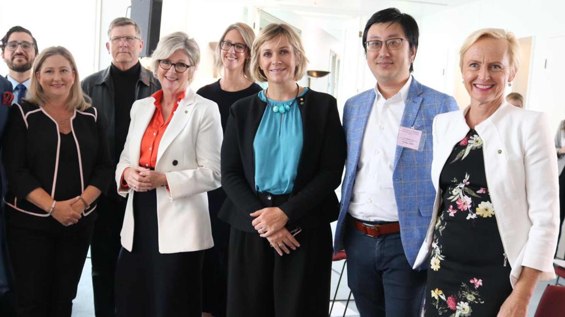 Photo of five women and three men in business -wear posing and smiling for a photo in a nondescript room