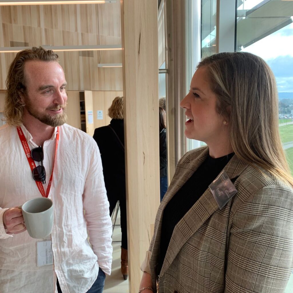 Bearded man in a casual white shirt holding a coffee cup chatting to a woman with long fair hair wearing a blazer