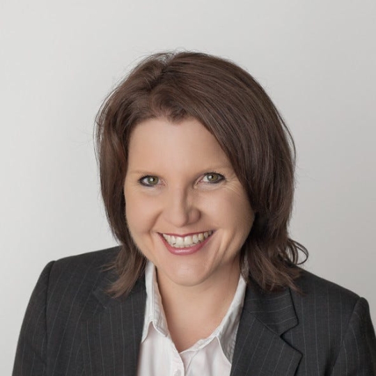 Photo of a brunette white woman smiling wearing grey blazer and white blouse