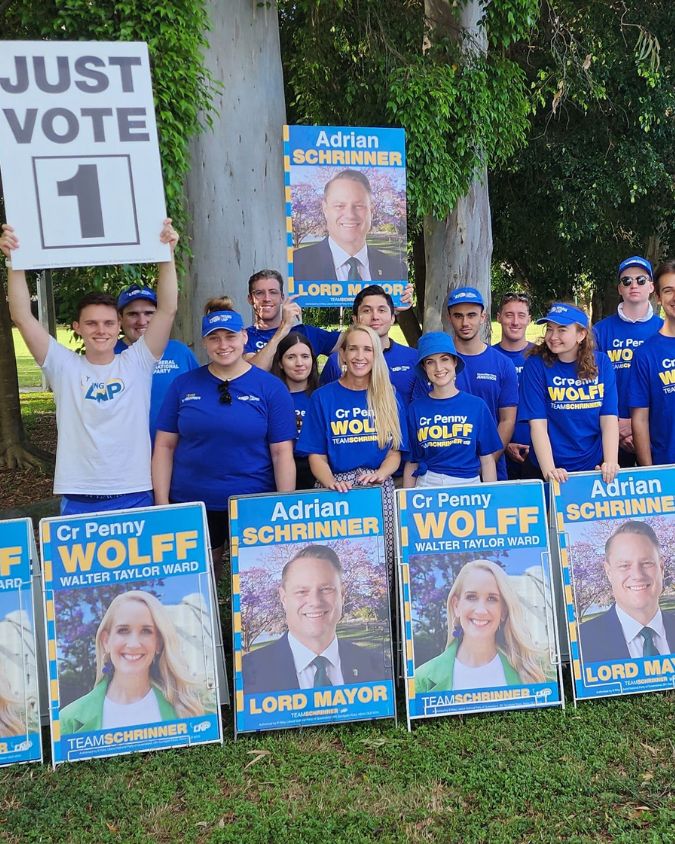 Crowd of people in blue tshirts holding "Penny Wolff" political placards