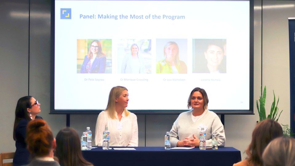 Three women on a panel, seated in front of a projector screen.
