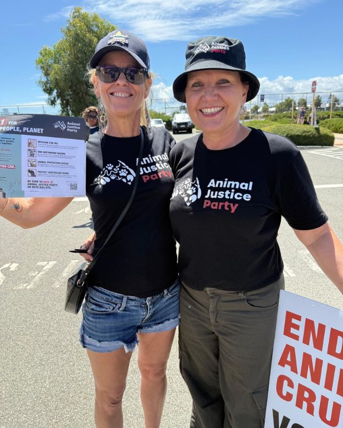 Two women wearing black animal justice t-shirts holding campaign brochures outdoors